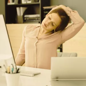 Woman exercising and stretching her neck at her home office, practicing good posture to prevent neck pain.